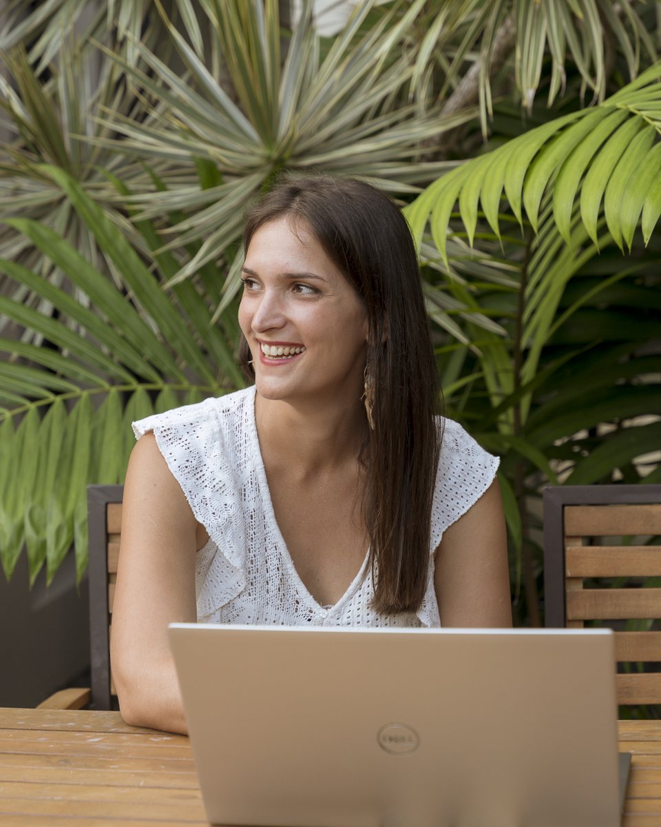 Aurélie, souriante, devant son ordinateur portable au milieu des palmiers