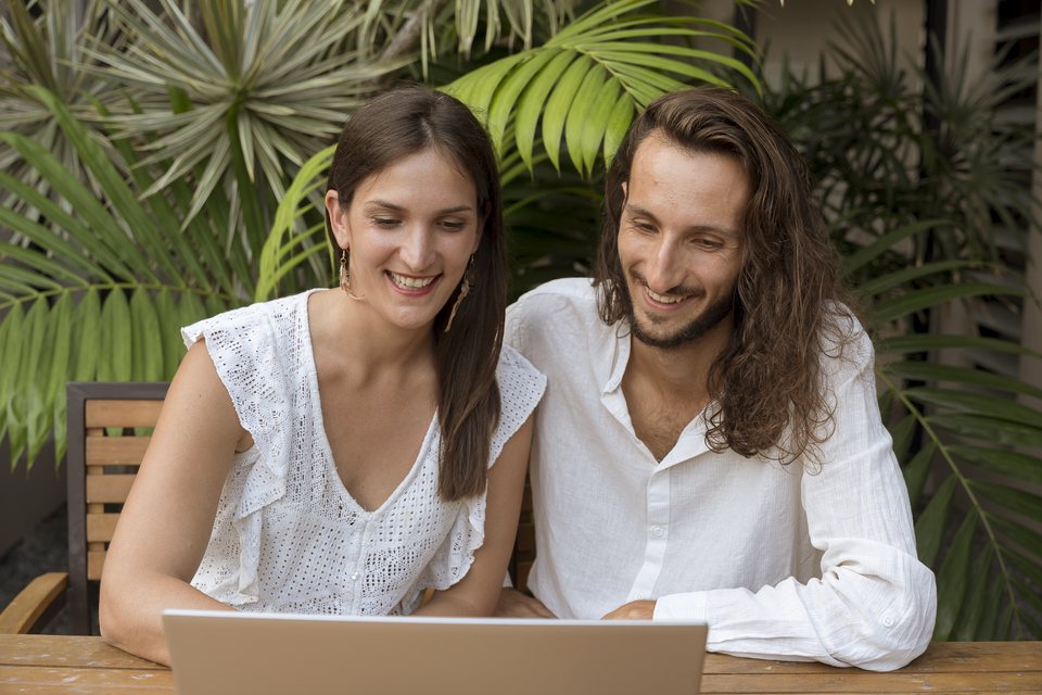Aurélie et Jonathan sourient devant leur ordinateur portable, au milieu des palmiers